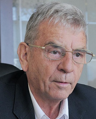 Gesicht eines älteren Mannes mit kurzem ergrauten Haar und Brille in einem Anzug
